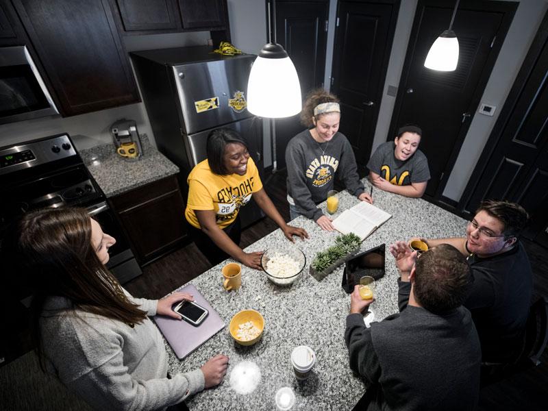 Group of students around an island in a kitchen in the Flats Apartments.